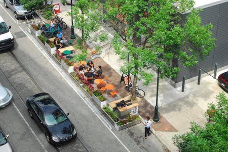 car parking spaces converted to outdoor eating area with trees, planter boxes, and people at tables and chairs